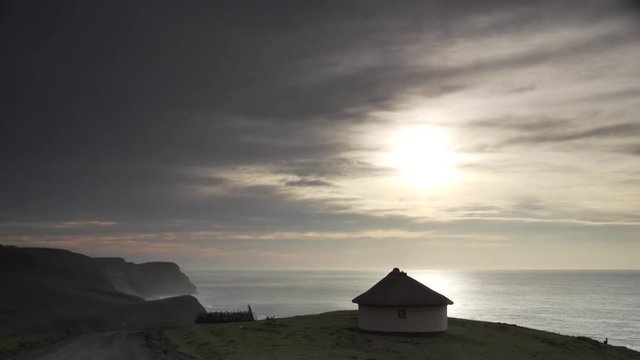 African mother and child silhouettes walking on a sand road at sunrise with a rickety fence and hut in the background soft clouds and sunlight in the background