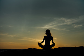 Silhouette meditation girl lotus position on stone on the background of the stunning sea.