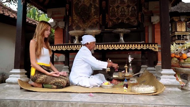 Old balinese priest performing praying ceremony with a young caucasian woman in small temple. Long shot with Sony a7s on slider