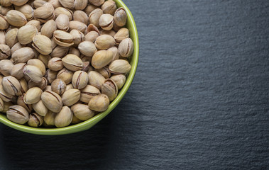 Pistachio nuts in a green plate on a dark background