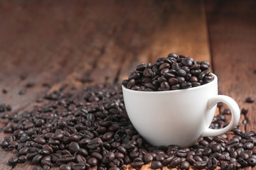 Close up shot of dark roasted coffee bean in white ceramic cup on wooden floor with copy space