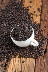 Close up shot of dark roasted coffee bean in white ceramic cup on wooden floor with copy space