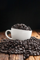 Close up shot of dark roasted coffee bean in white ceramic cup on wooden floor with copy space