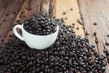 Close up shot of dark roasted coffee bean in white ceramic cup on wooden floor with copy space and warm tone processed