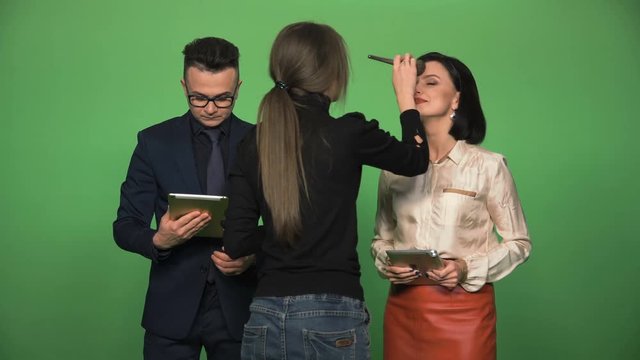 Man and woman getting prepared by visagiste and then speaking at camera with tablets.