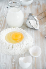 Ingredients and tools for baking - flour, eggs and glass of milk on the wooden rustic table background, selective focus