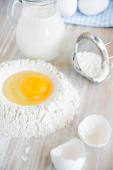 Ingredients and tools for baking - flour, eggs and glass of milk on the wooden rustic table background, selective focus