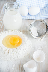 Ingredients and tools for baking - flour, eggs and glass of milk on the wooden rustic table background, selective focus