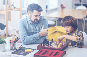 Cute boy playing chess with his father