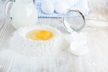Ingredients and tools for baking - flour, eggs and glass of milk on the wooden rustic table background, selective focus