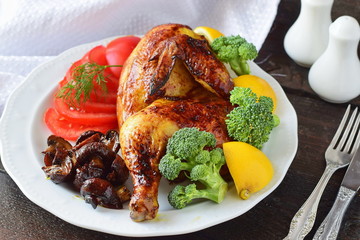 Roasted chicken half with boiled broccoli, sliced tomato, lemon and fried mushrooms on a white plate. Ready to serve dish. Cooking step by step. Healthy eating concept