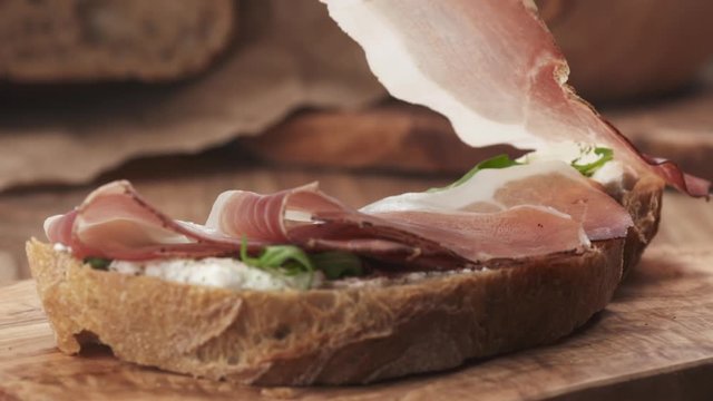 Slow motion of italian speck put on rustic bread with arugula and ricotta cheese, 180fps prores footage