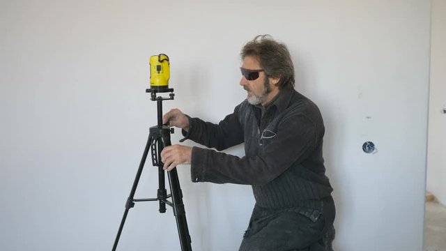 Working with a laser level makes markings on the wall. Mechanical lifting. Violent emotions