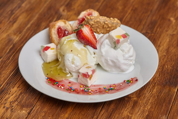 Ice cream on plate with strawberry, syrup and other treats