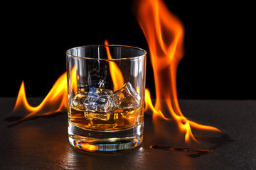 glass of whiskey with ice on a background of a burning flame