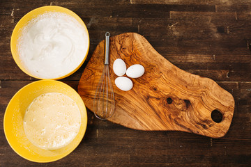 Eggs on wooden board, bowls with cake ingredients