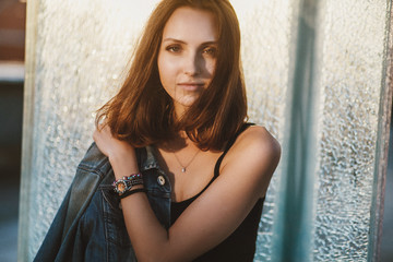 Obraz premium Lifestyle Portrait of young beautiful woman with river background. Girl in jeans shorts and a jacket standing in a sunny bright light