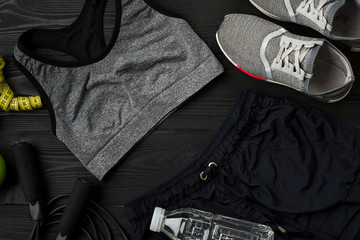 Athlete's set with female clothing, sneakers and bottle of water on dark background