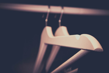Four blank wooden hangers in a dark wardrobe, black background.  