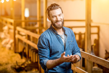 Portrait of a handsome businessman farmer standing in the barn with goats. Natural milk production and farming