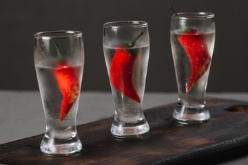 Cold vodka in a shot glass on a wooden cutting board on dark background