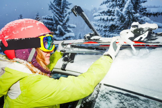 Female skier fastening skis to roof rails of car