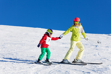 Mother teaching kid son skiing in snowy mountains
