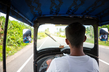 Tuk tuk driver on road of Sri Lanka, view from car