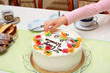 Dłoń dziewczynki zabiera ozdoby z tortu urodzinowego. - obrazy, fototapety, plakaty