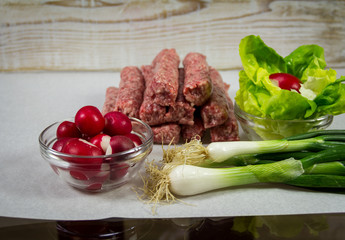 Raw kebab minced meat, lettuce, radishes and green onions, on white paper for grilling