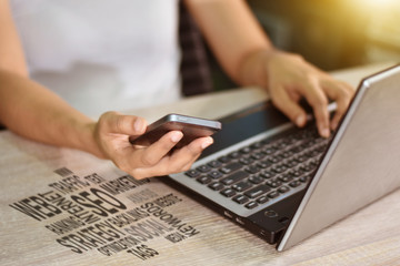 A woman's hand working on a laptop computer and interactive technology online on a smartphone.