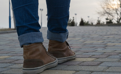 Legs of a girl in brown sneakers and jeans walking along an avenue with a park on the horizon
