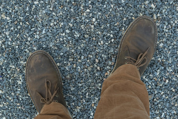 Men's legs in leather brown shoes and mustard-colored trousers on a path lined with fine gravel