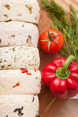Variety of home made cheese and paprica and herbs on a wooden board. brined curd white cheese with vegetables.