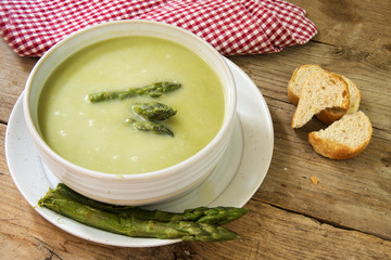 soup from green asparagus in a bowl, napkin and bread on a rustik wooden table