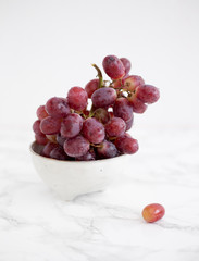 Red grapes in rustic bowl on a white marble background. Vine concept