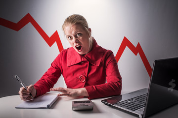 Angry and mad young or middle aged woman at work sitting at desk working.