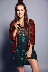 Beautiful caucasian smiling hipster brunette woman model in bright shinny reflecting summer stylish jacket and green dress posing on gray background. Eating french macaroon