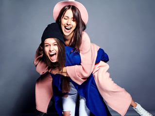 fashion portrait of two smiling brunette women models in summer casual hipster overcoat posing on gray background. Girls holding each other on back