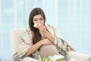 Pregnant woman with allergy sitting on armchair at home