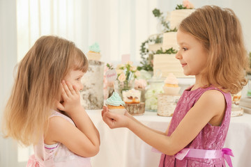 Obraz na płótnie Canvas Cute girl giving tasty cupcake to her friend at party