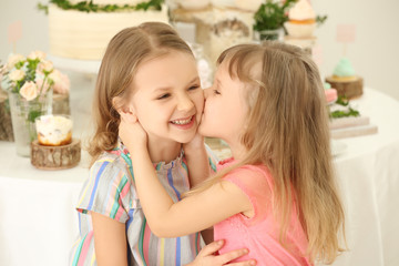 Cute little girls near table with sweets served for party