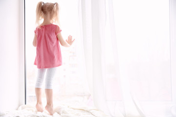 Cute little girl standing on windowsill