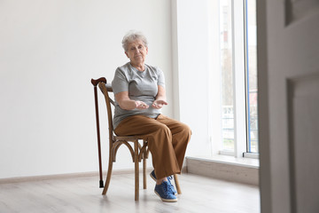 Senior woman counting coins while sitting on chair in empty room. Poverty concept