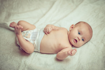 happy baby lying on white sheet and holding his legs