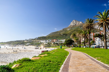 Beautiful evening view of Lion's Head Mountain in Cape Town, South Africa, seen from the seafront esplanade in Camps Bay. White sand beach, evening sun and palm trees along the promenade.