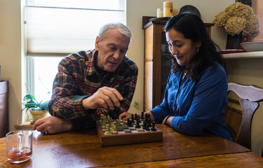 young woman playing chess with senior man providing companionship, improving ones health 
