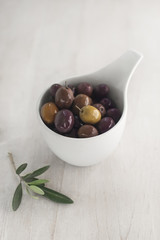 Kalamata olives and olive branch on a light wooden background