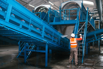 The worker washes the equipment at the waste sorting plant. Waste processing plant. Technological process. Recycling and storage of waste for further disposal.