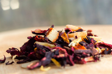 Pile of fruit tea with petals and dry fruit .The composition of the heap of tea leaves and dried hibiscus flower located on a wooden Board. Tea with natural ingredients closeup. Macro photo of tea.